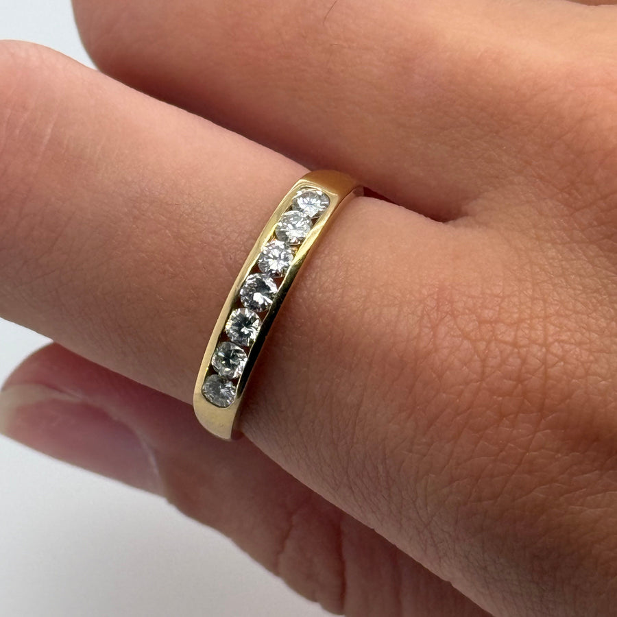 Gold ring with embedded diamonds on a finger against a neutral background