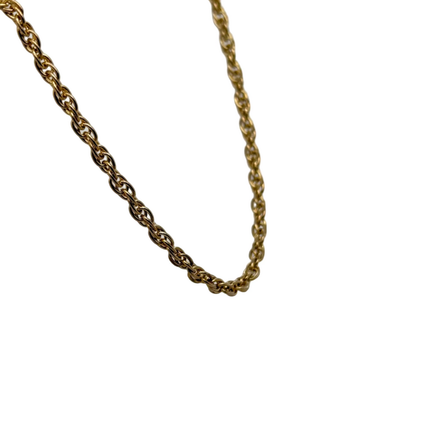 Gold chain necklace on a white stand with a gray background
