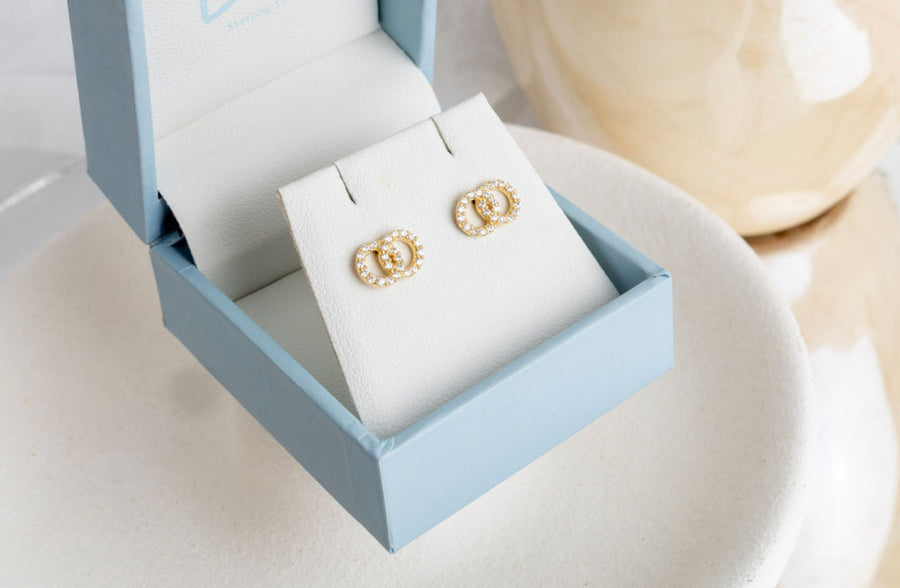 Gold earrings in a light blue jewelry box with 'Dew' branding.